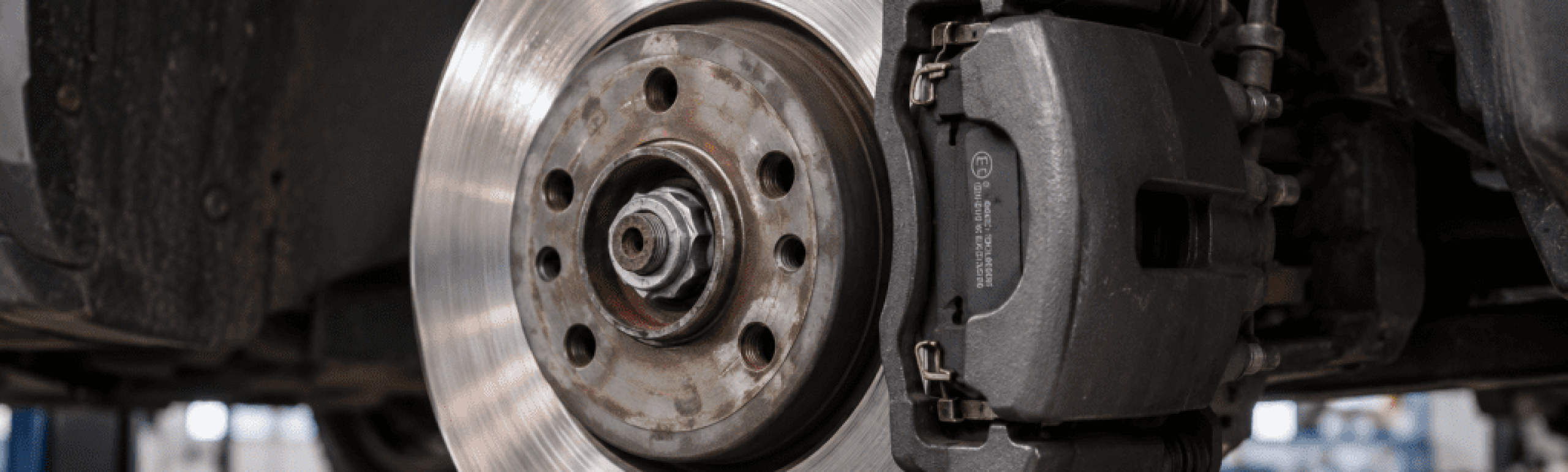 Nahaufnahme der Scheibenbremsanlage eines Autos, die die Bremsscheibe aus Metall und den Bremssattel zeigt. Der Hintergrund in der Werkstatt deutet auf die Diagnose „Bremsen quietschen“ hin – mit Schwerpunkt auf Ursachen und Lösungen für quietschende Bremsen.